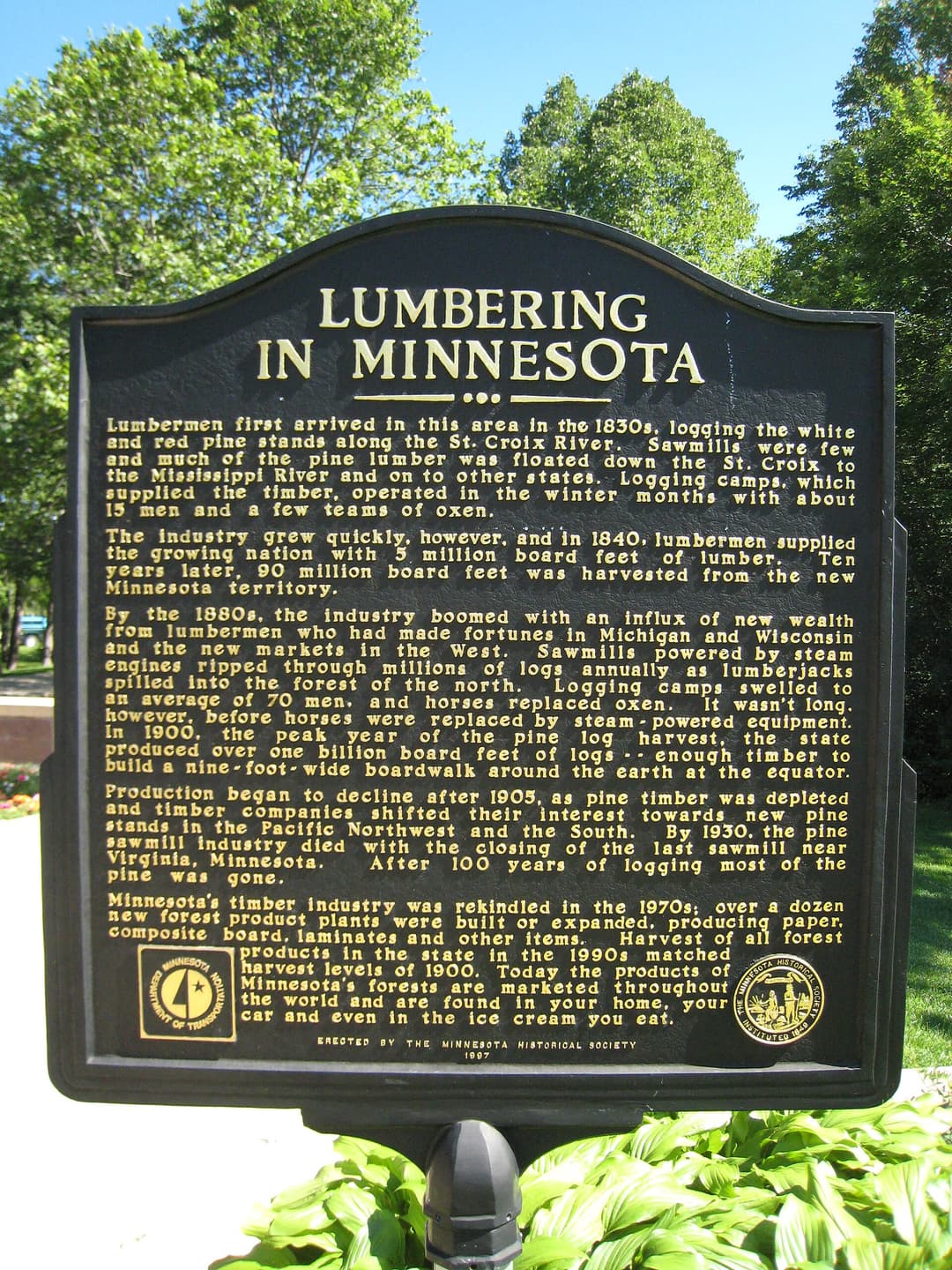 Historic marker, Lumbering in Minnesota Kettle River, at a rest area in Minnesota, United States.
TEXT: Lumbering first arrived in this area in the 1830s, logging the white and red pine stands along the St. Croix River. Sawmills were few and much of the pine lumber was floated down the St. Croix to the Mississippi River and on to other states. Logging camps, which supplied the timber, operated in the winter months with about 15 men and a few teams of oxen.
The industry grew quickly, however, and in 1840, lumbermen supplied the growing nation with 5 million board feet of lumber. Ten years later, 90 million board feet was harvested from the new Minnesota territory.
By the 1880s, the industry boomed with an influx of new wealth from lumbermen who had made fortunes in Michigan and Wisconsin and the new markets in the West. Sawmills powered by steam engines ripped through millions of logs annually as lumberjacks spilled into the forests of the north. Logging camps swelled to an average of 70 men, and horses replaced oxen. It wasn't long, however, before horses were replaced by steam-powered equipment. In 1900, the peak year of the pine log harvest, the state produced over one billion board feet of logs--enough timber to build a nine-foot-wide boardwalk around the earth at the equator.
Production began to decline after 1905, as pine timber was depleted and timber companies shifted their interest towards new pine stands in the Pacific Northwest and the South. By 1930, the pine sawmill industry died with the closing of the last sawmill near Virginia, Minnesota. After 100 years of logging most of the pine was gone.

Minnesota's timber industry was rekindled in the 1970s; over a dozen new forest product plants were built or expanded, producing paper, composite board, laminates and other items. Harvest of all forest products in the state in the 1990s matched harvest levels of 1900. Today the products of Minnesota's forests are marketed throughout the world and are found in your home, your car and even in the ice cream you eat.